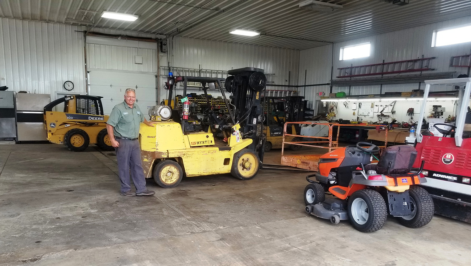 Chicago Rental & Repair owner Perry posing inside shop with forklifts and other equipment to be repaired - Lincoln, IL